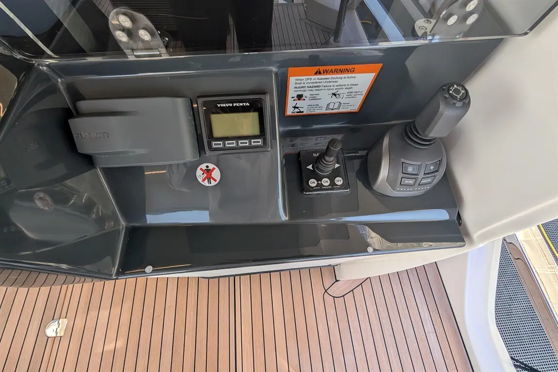 Control panel on a boat featuring Volvo Penta display, joystick, Fusion compartment, safety warning label, and wooden deck.